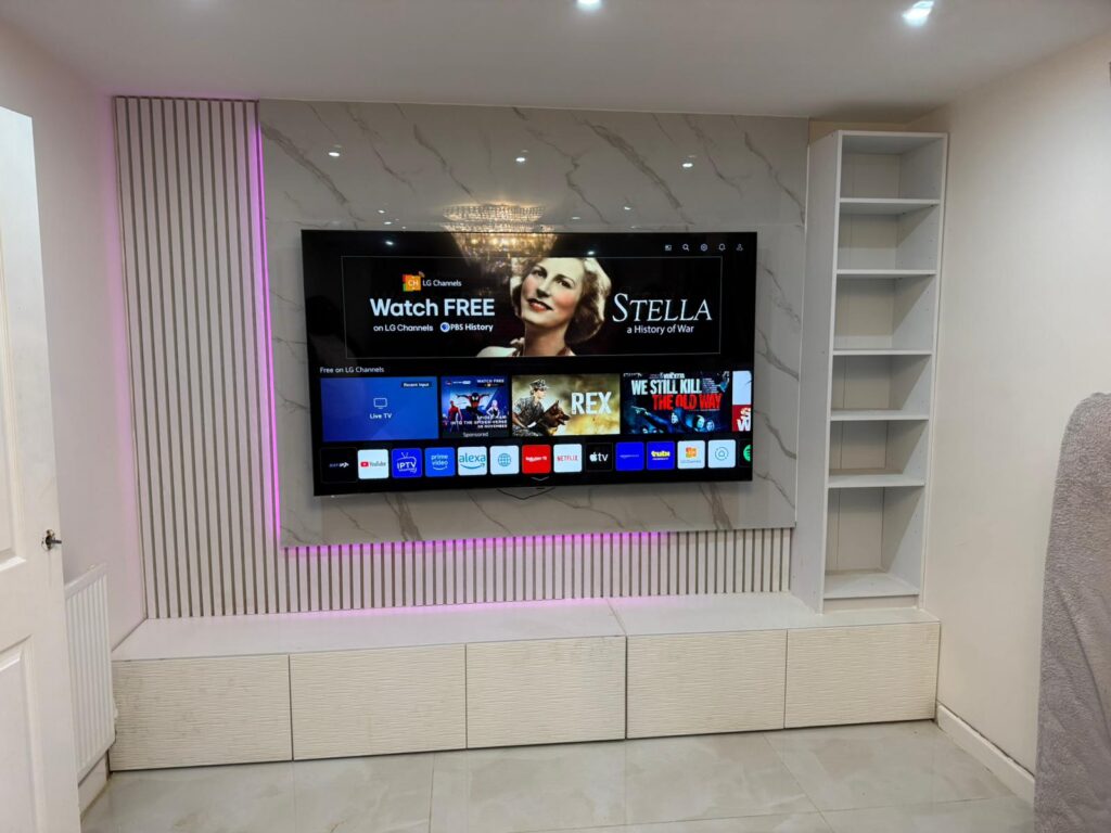 Contemporary media wall with a large mounted TV, marble-effect paneling, vertical slat feature with pink LED lighting, built-in shelving, and low storage cabinets in a modern minimalist living room.