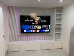 Contemporary media wall with a large mounted TV, marble-effect paneling, vertical slat feature with pink LED lighting, built-in shelving, and low storage cabinets in a modern minimalist living room.